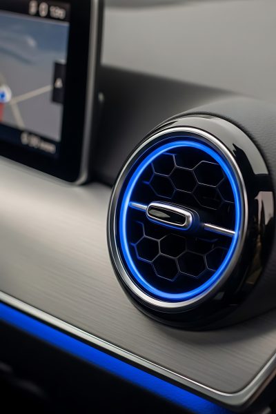 Close up of a car dashboard with a blue lit air vent and a navigation screen visible on the left